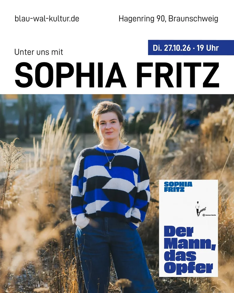 Portrait of a woman in a blue‑black‑white striped sweater and jeans standing in tall dry grass, looking forward.