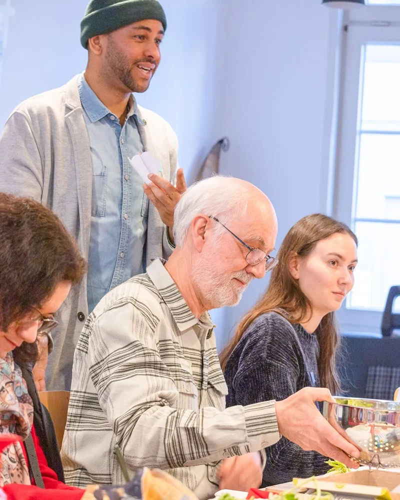 Group of people at a table with fruit, markers, and a bowl, participating in a workshop.