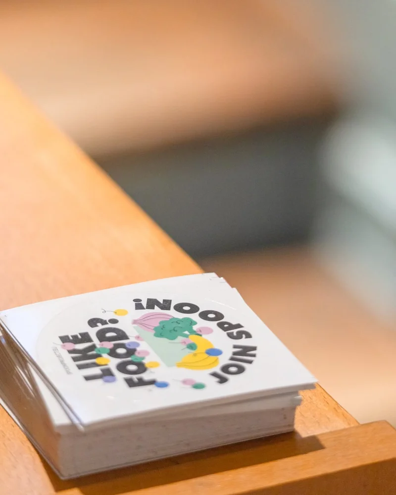 Stack of stickers showing 'LIKE FOOD? JOIN US' with illustrated vegetables and fruit.